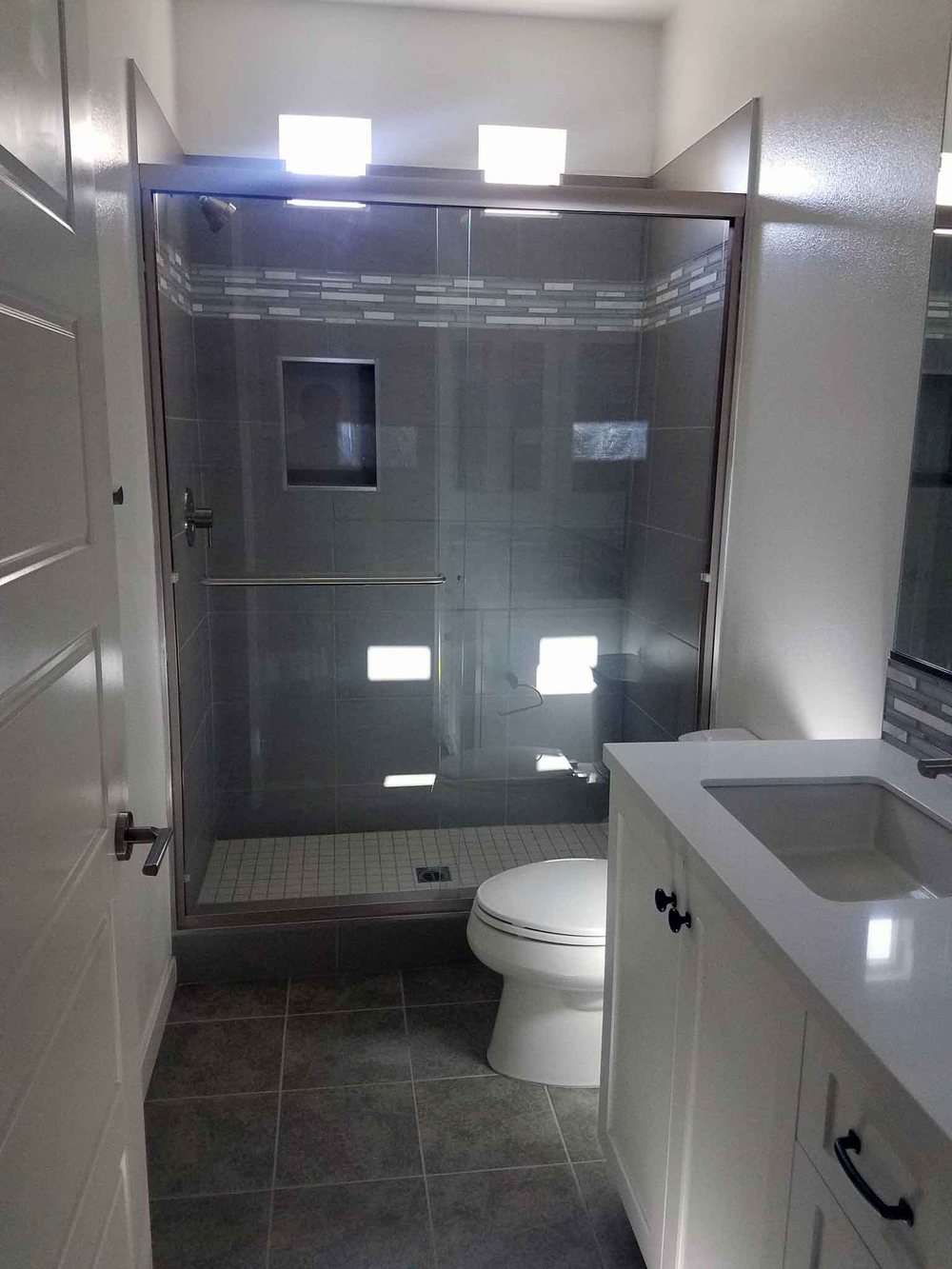 Remodeled bathroom with glass shower enclosure and gray tile