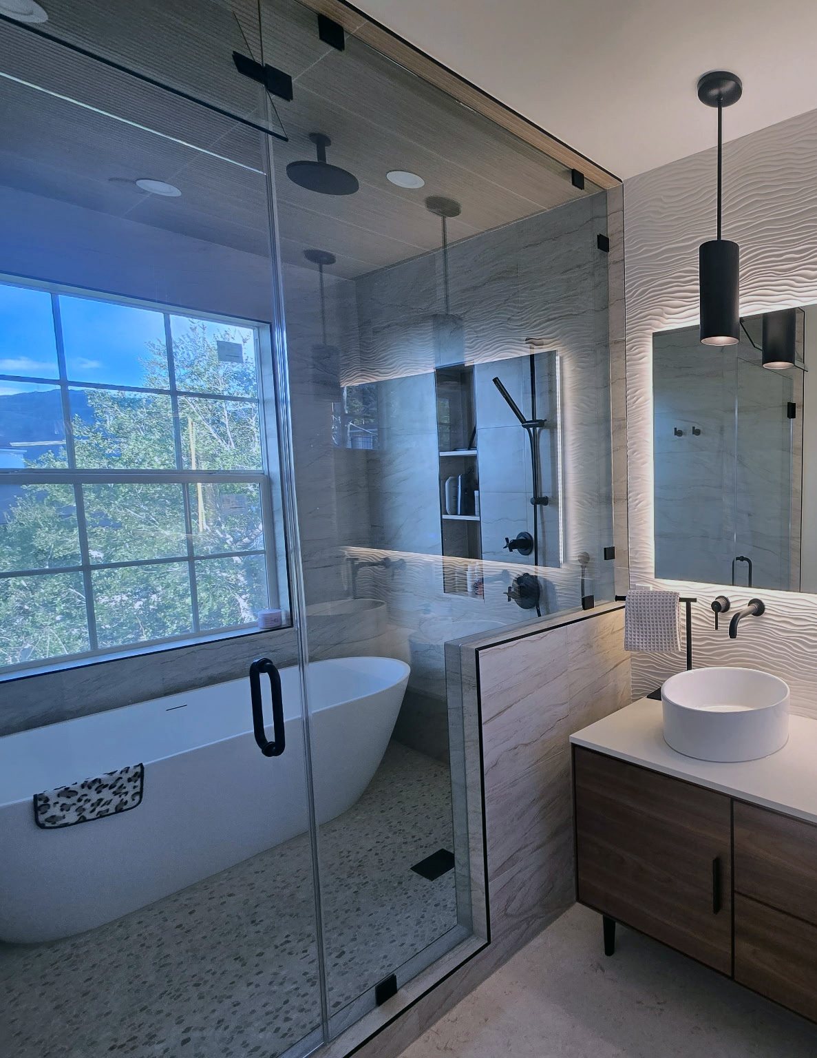Modern remodeled bathroom with freestanding tub and glass shower, wave-textured accent wall